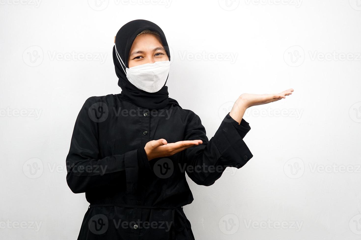 Mujer musulmana con máscara blanca, con la mano apuntando al espacio vacío presentando algo, aislado sobre fondo blanco. foto