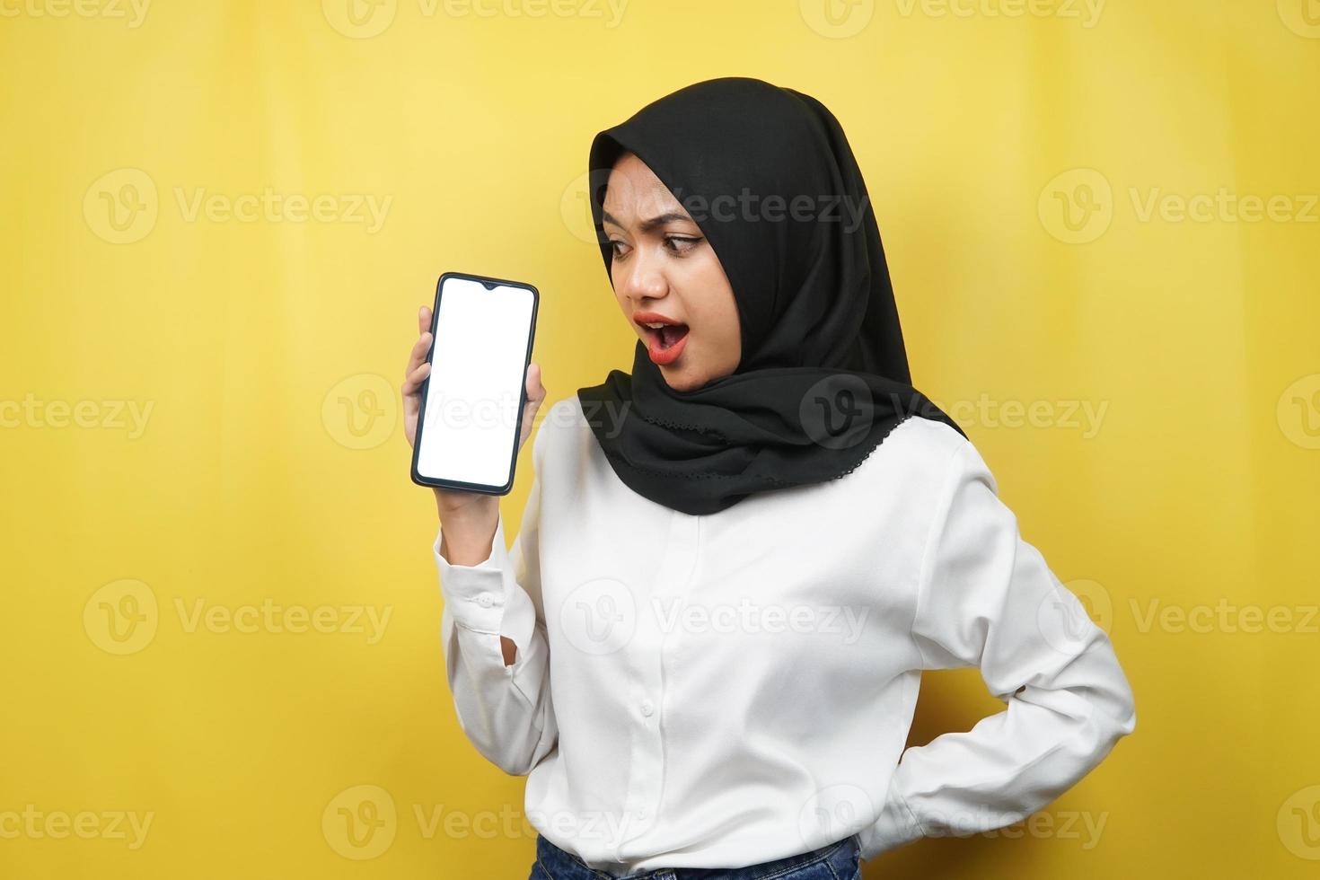 Beautiful young asian muslim woman shocked, surprised, wow expression, hand holding smartphone with white or blank screen, promoting app, promoting product, presenting something, isolated photo