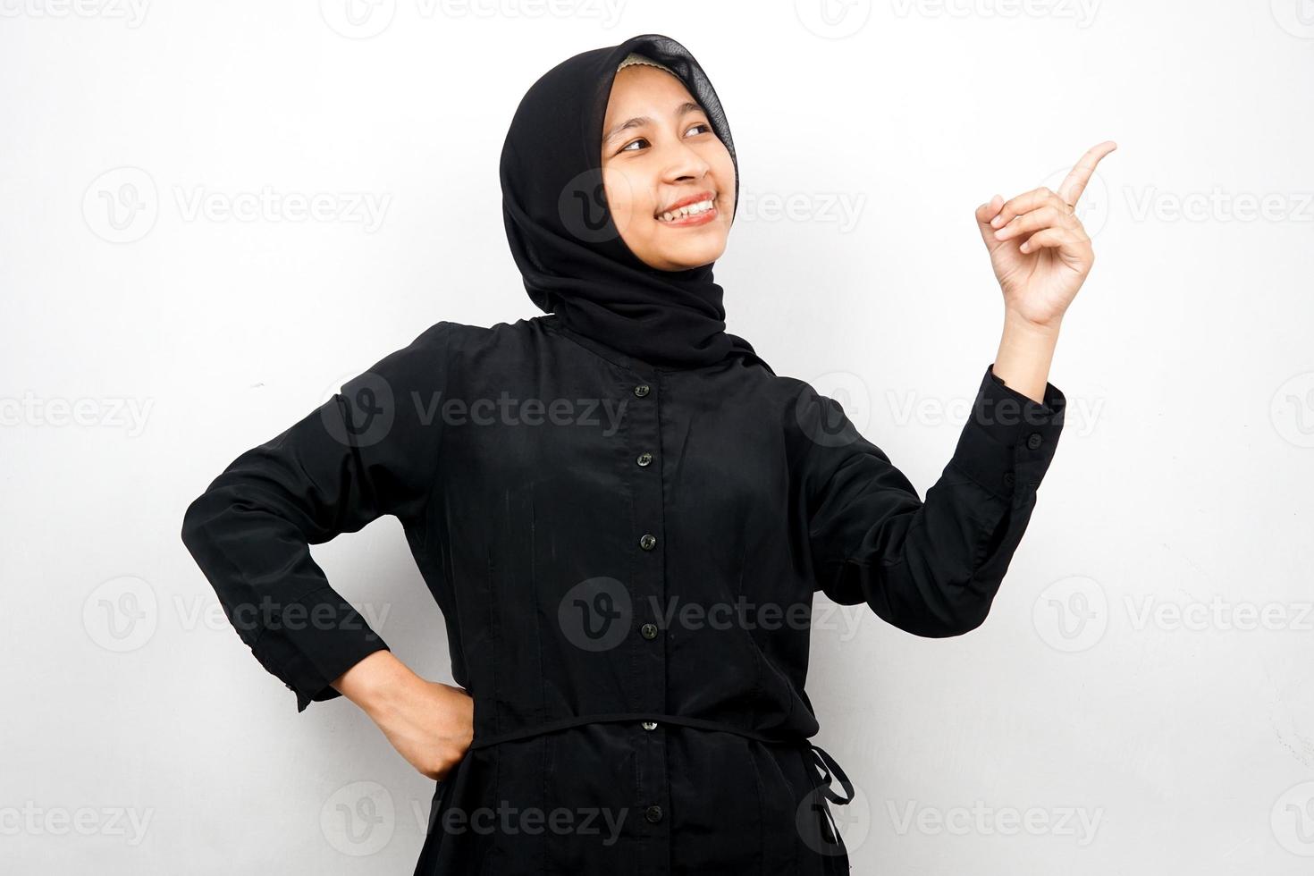 Hermosa y alegre joven musulmana asiática, con la mano apuntando al espacio vacío, presentando algo, aislado sobre fondo blanco. foto