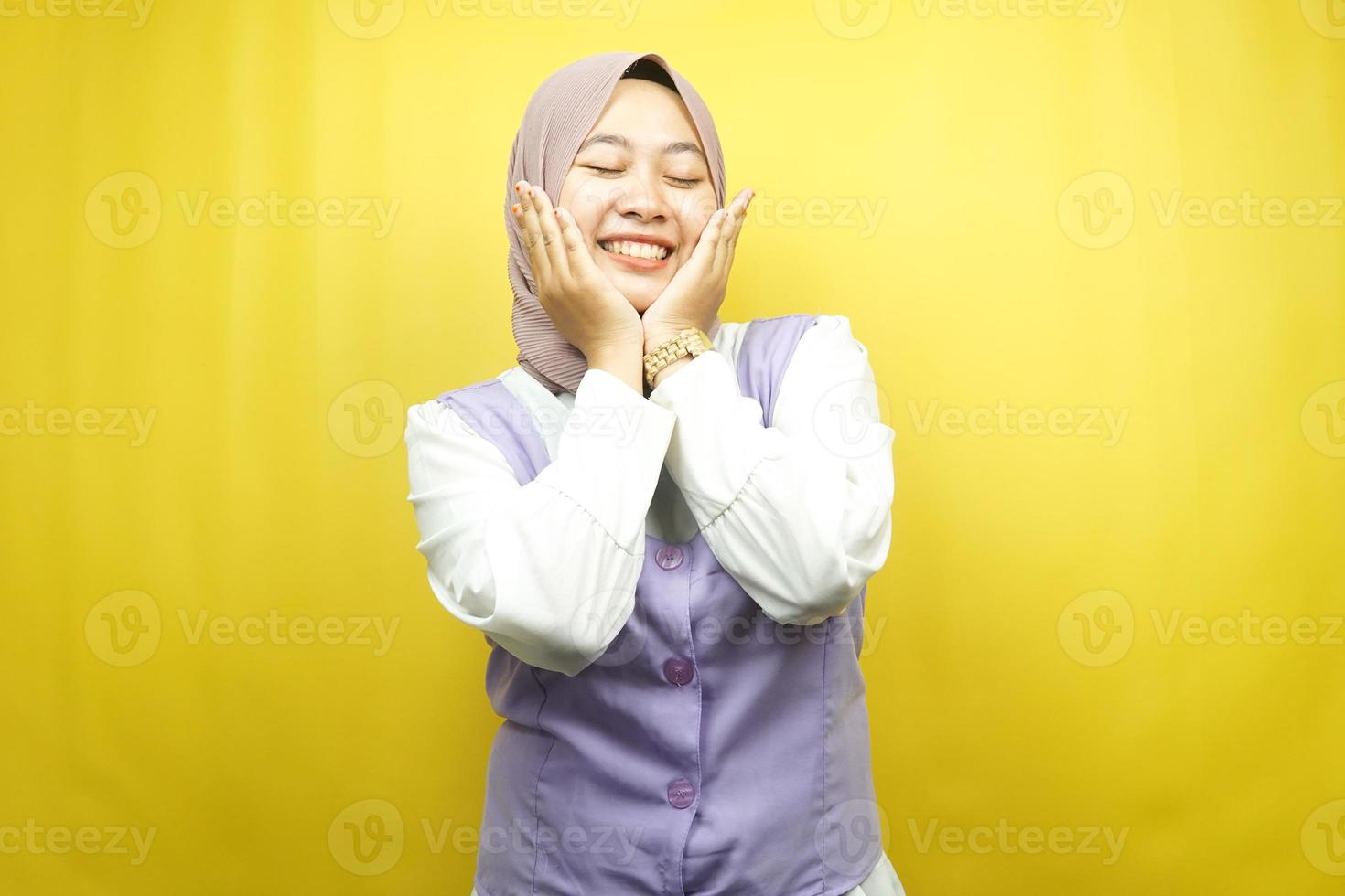 Hermosa joven musulmana asiática sonriendo feliz, linda, sintiéndose cómoda, sintiéndose cuidada, sintiéndose bien, con las manos sosteniendo las mejillas aisladas sobre fondo amarillo foto