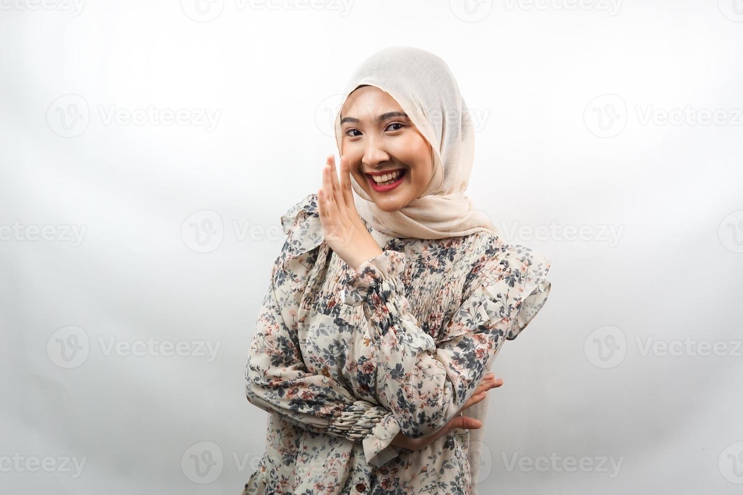 Beautiful young asian muslim woman smiling confidently and excitedly close to camera, whispering, telling secrets, speaking quietly, silent, isolated on white background photo