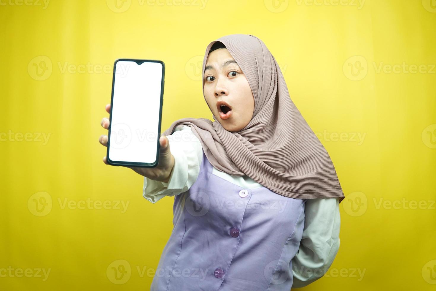 Hermosa joven mujer musulmana asiática conmocionada, sorprendida, expresión guau, mano sosteniendo un teléfono inteligente con pantalla blanca o en blanco, promocionando la aplicación, promocionando el producto, presentando algo, aislado foto