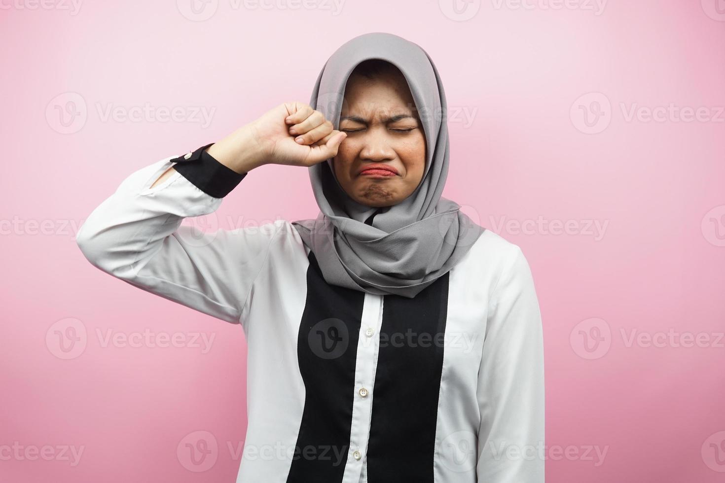 Beautiful young muslim woman crying, hands wiping tears, isolated on pink background photo