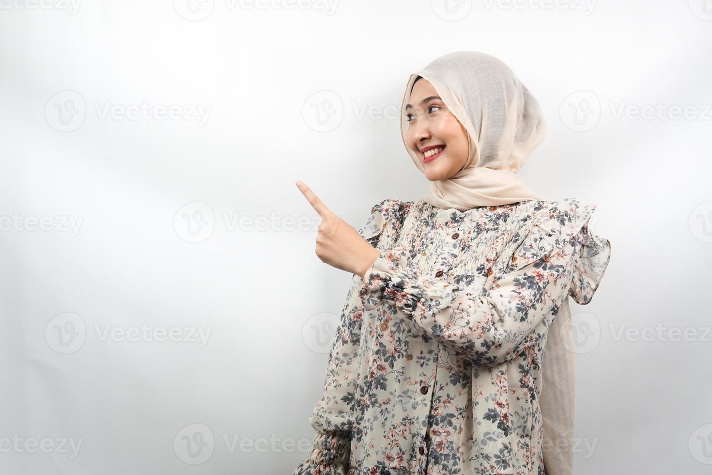 Hermosa joven musulmana asiática con las manos apuntando hacia el espacio vacío presentando algo, sonriendo confiado, entusiasta, alegre, frente al espacio vacío, aislado sobre fondo blanco. foto