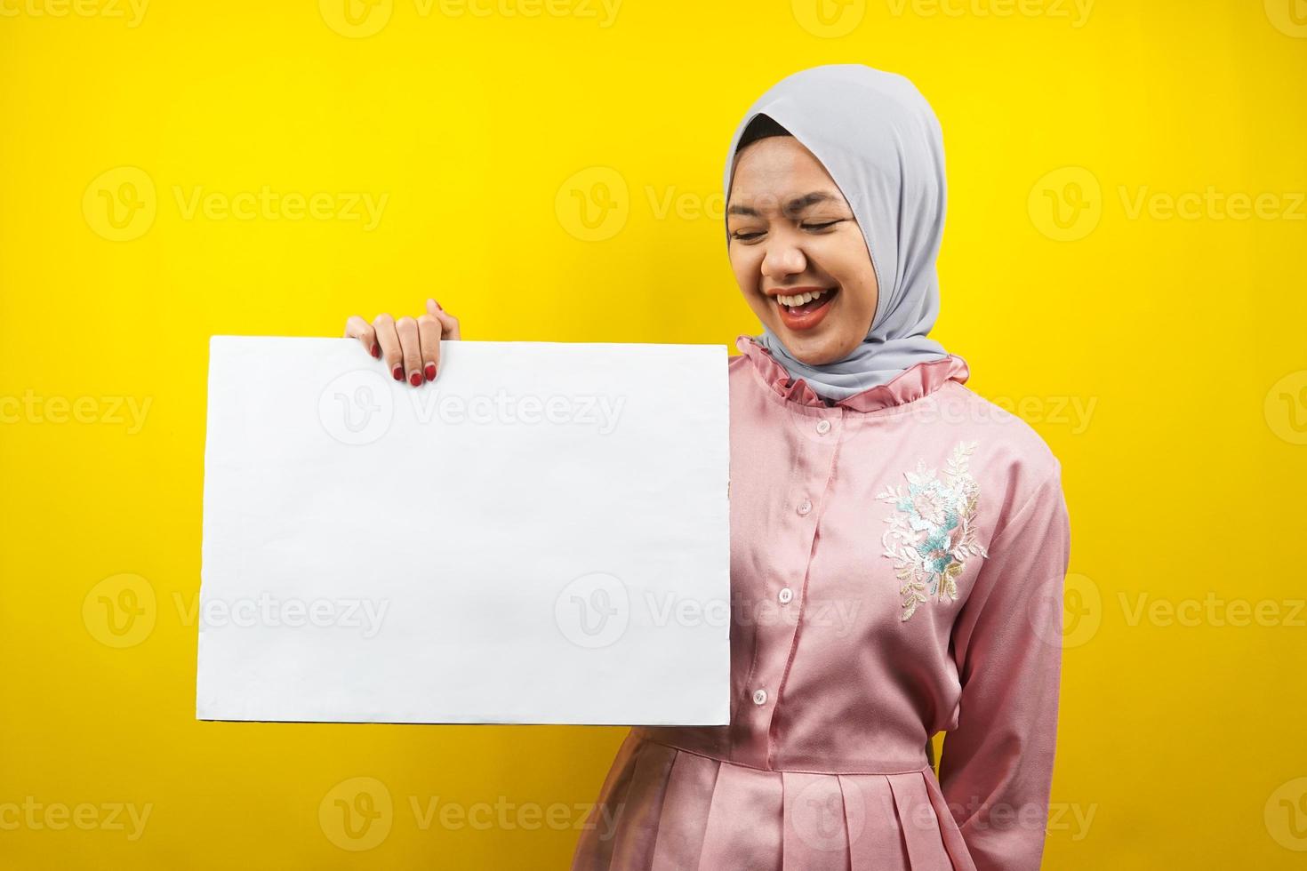 Bastante joven mujer musulmana alegre sosteniendo pancarta vacía en blanco, cartel, tablero blanco, tablero de letrero en blanco, tablero de anuncio blanco, presentando algo en el espacio de la copia, promoción foto