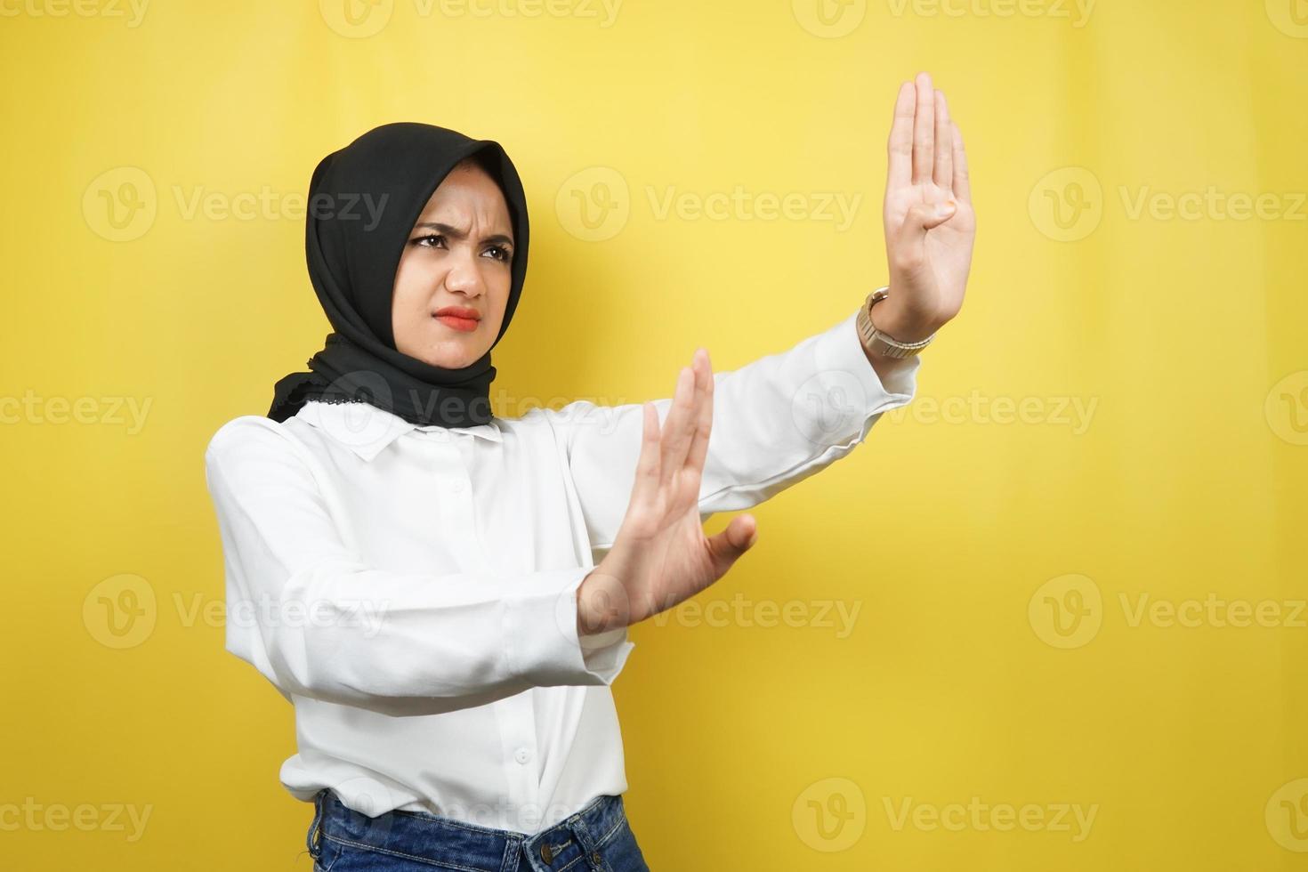 Hermosa joven musulmana asiática con la mano rechazando algo, la mano deteniendo algo, disgustando algo en el espacio vacío, aislado sobre fondo amarillo foto
