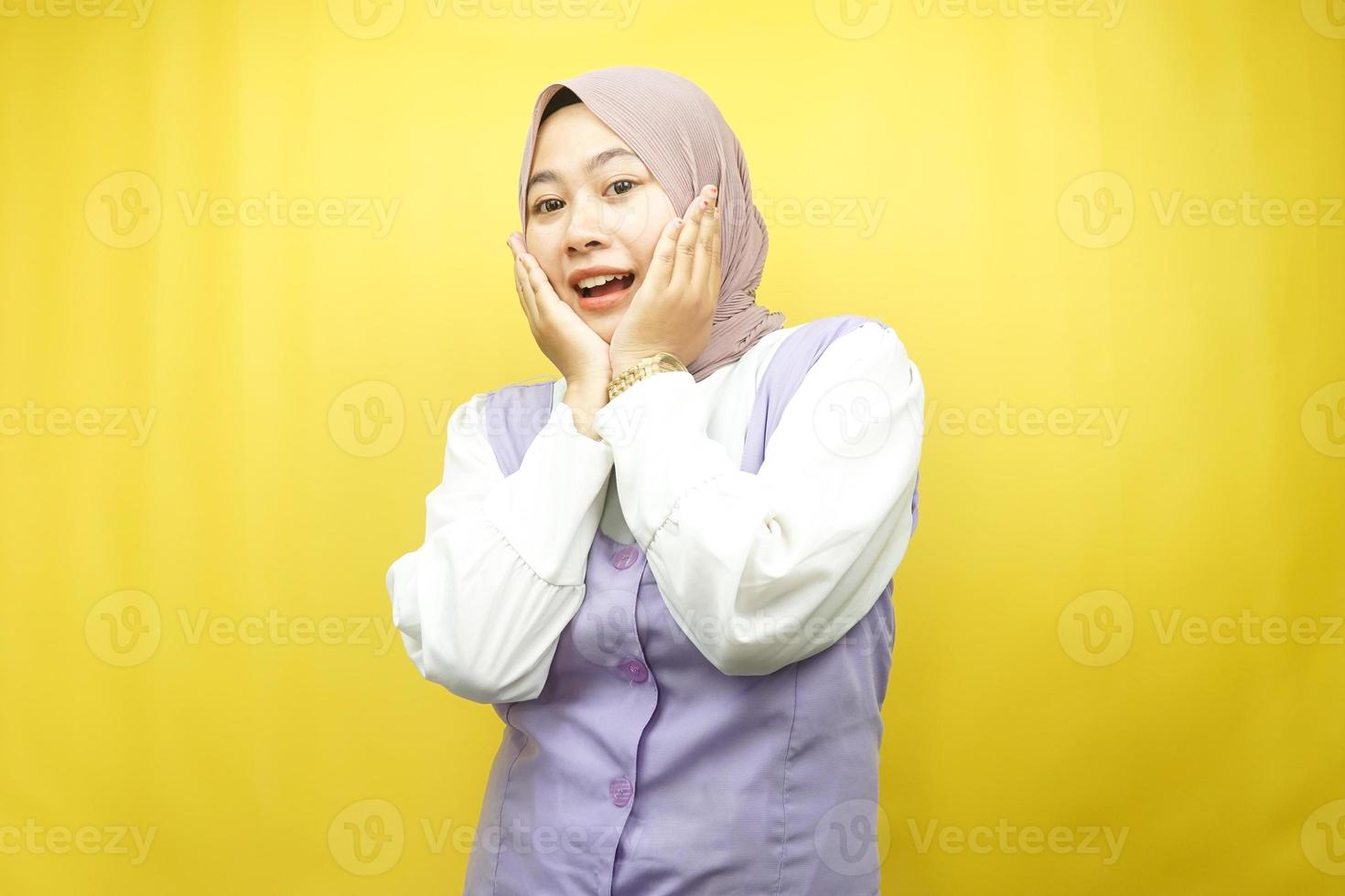 Beautiful young asian muslim woman shocked, surprised, wow expression, with hand holding cheek facing camera isolated on yellow background photo