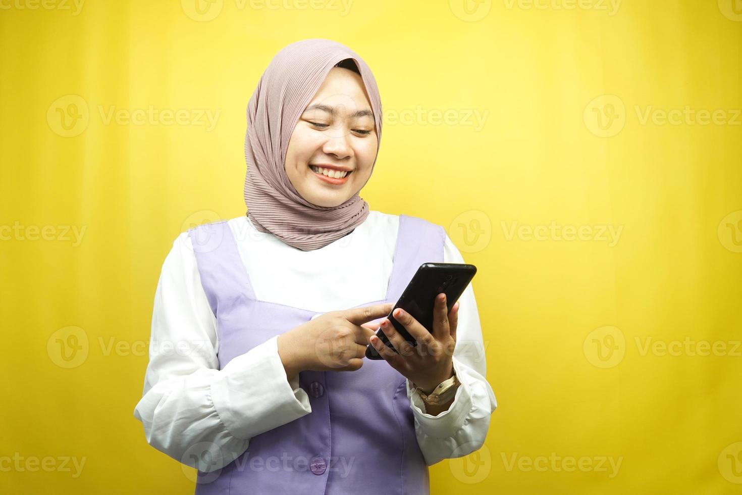 Hermosa joven mujer musulmana asiática sonriendo con confianza sosteniendo smartphone aislado sobre fondo amarillo, concepto de publicidad foto