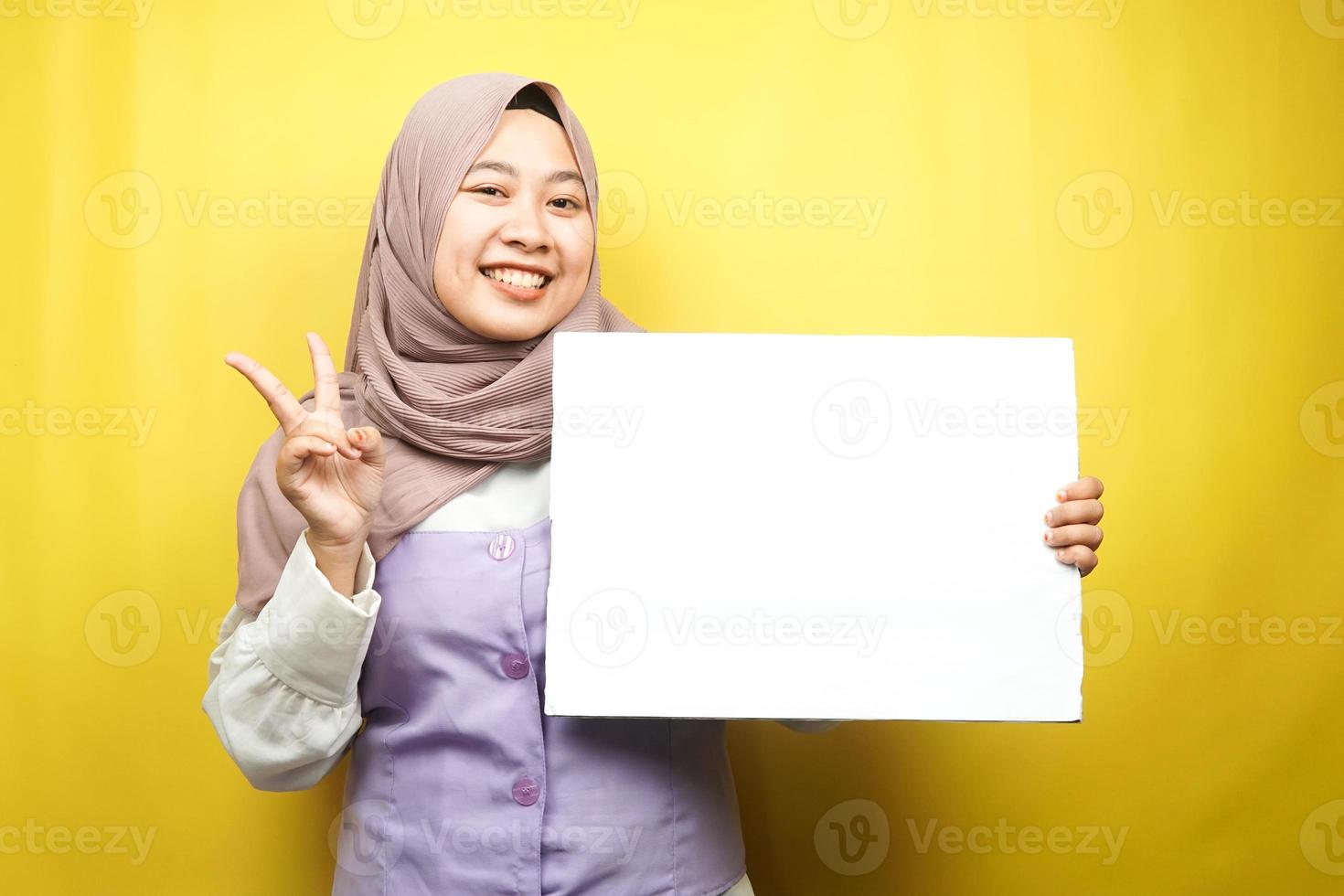 Bastante joven mujer musulmana alegre sosteniendo pancarta vacía en blanco, cartel, tablero blanco, tablero de letrero en blanco, tablero de anuncio blanco, presentando algo en el espacio de la copia, promoción foto