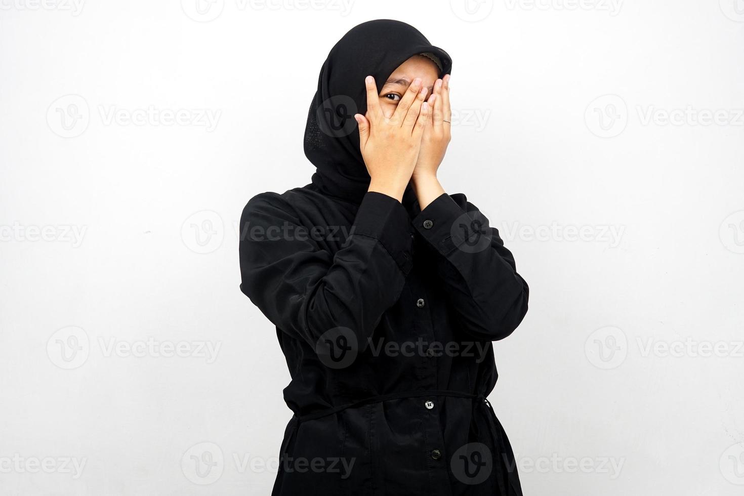 Beautiful young asian muslim woman with eyes peeking between fingers, isolated on white background photo