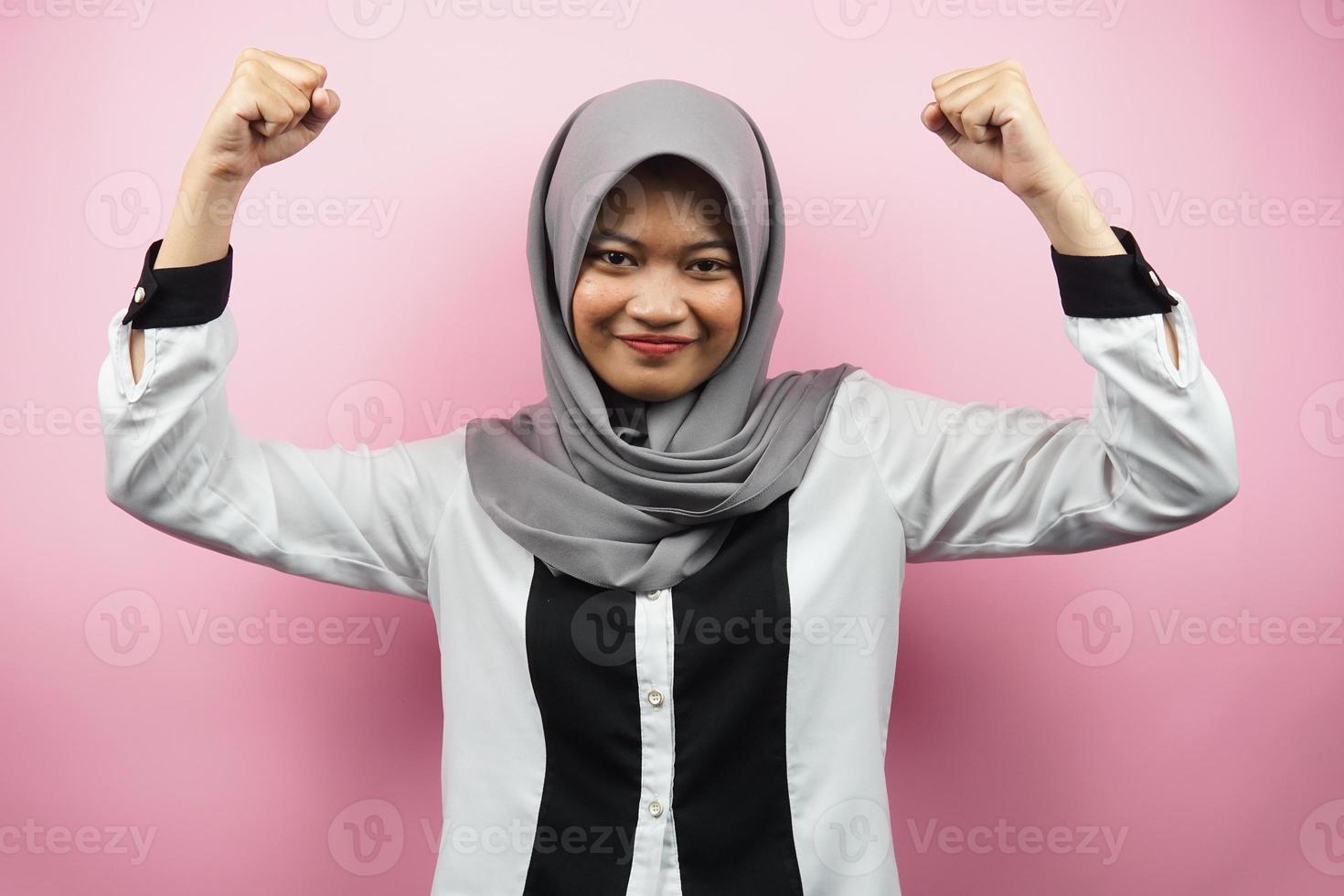 Hermosa joven musulmana asiática con músculos levantados, brazos de signo de fuerza, aislado sobre fondo de color rosa foto