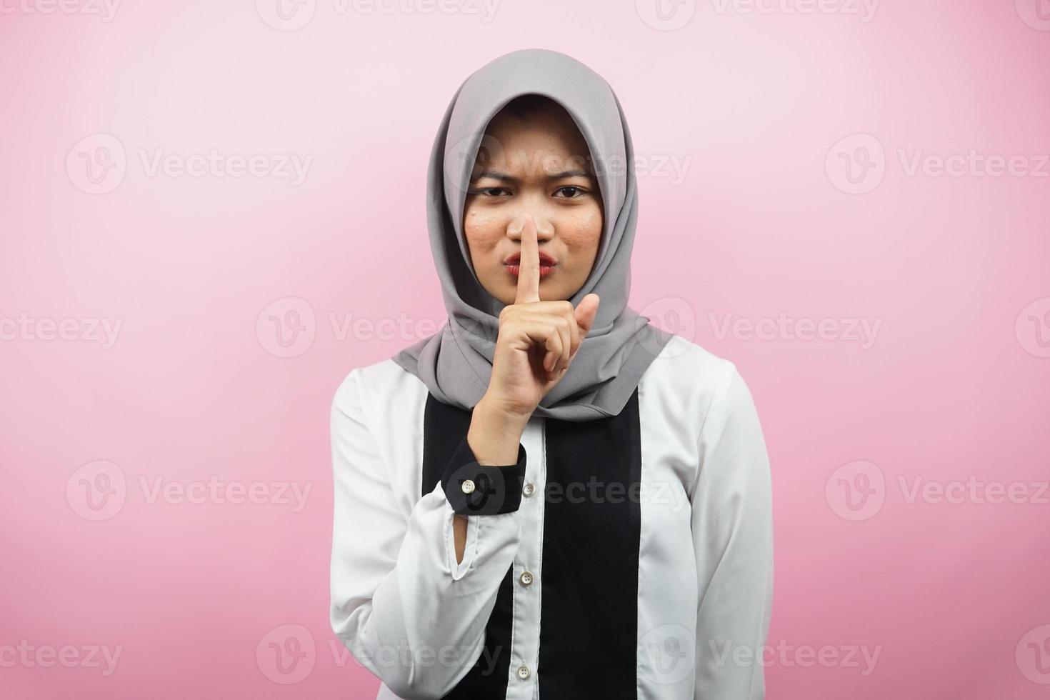 Beautiful asian young muslim woman with finger on mouth, telling to be quiet, don't make noise, lower your voice, don't talk, isolated on pink background photo