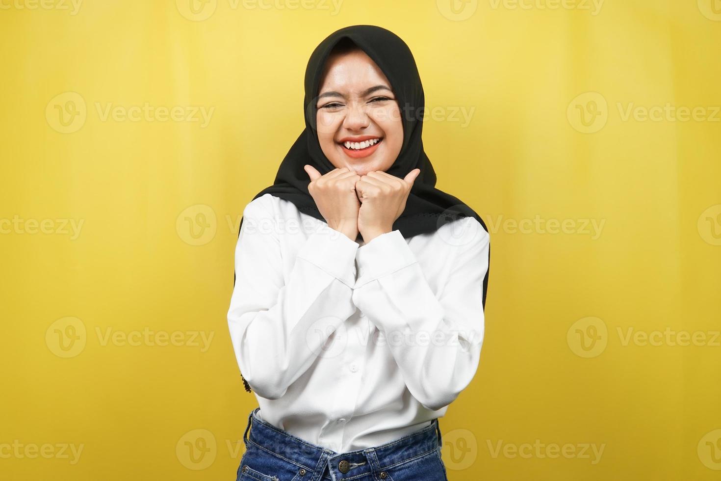 Hermosa joven mujer musulmana asiática sonriendo feliz, linda, sintiéndose cómoda, sintiéndose cuidada, sintiéndose bien, con las manos sosteniendo la barbilla aislada sobre fondo amarillo foto