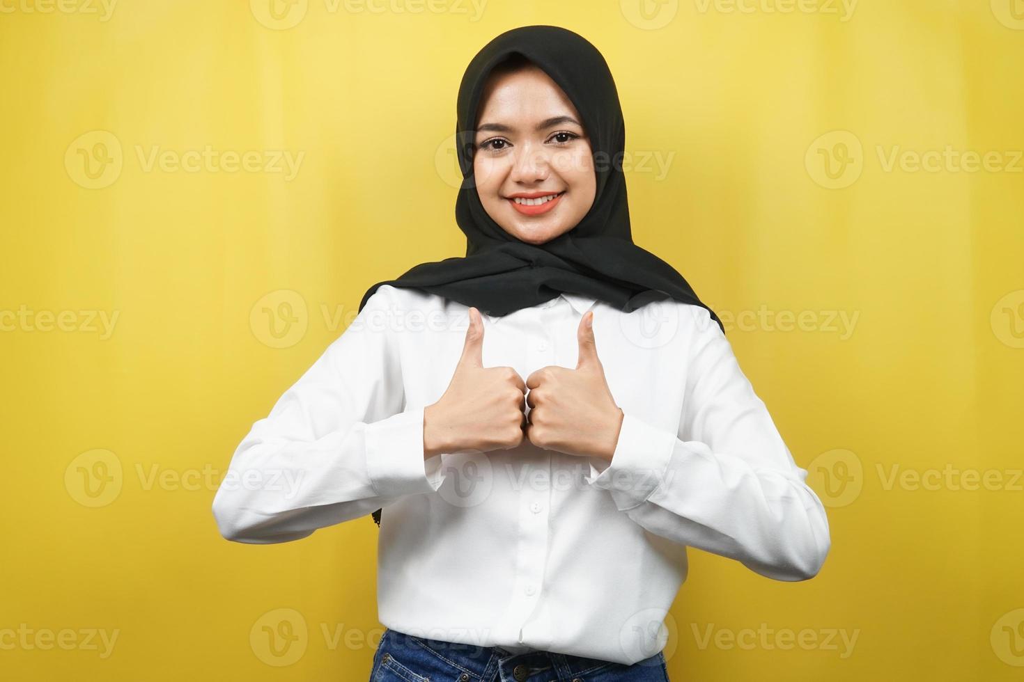 Hermosa joven musulmana asiática con las manos pulgares arriba, signo de ok, buen trabajo, éxito, victoria, sonriendo confiado, entusiasta y alegre, mirando a cámara aislada sobre fondo amarillo foto