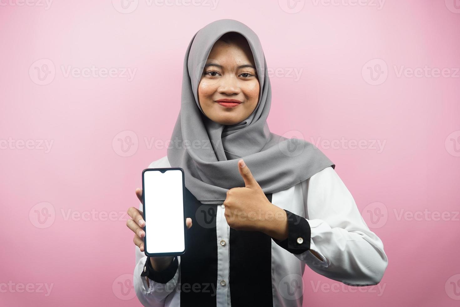 Hermosa joven musulmana asiática sonriendo con confianza y entusiasmo con las manos sosteniendo el teléfono inteligente, presentando la solicitud, mano de signo ok, buen trabajo, éxito, aislado sobre fondo rosa foto