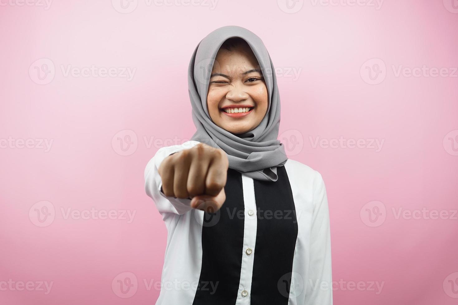 Beautiful young asian muslim woman smiling confident, enthusiastic and cheerful with fists clenched at camera, punching, fighting, cooperation, eyes glinting, looking at camera isolated photo