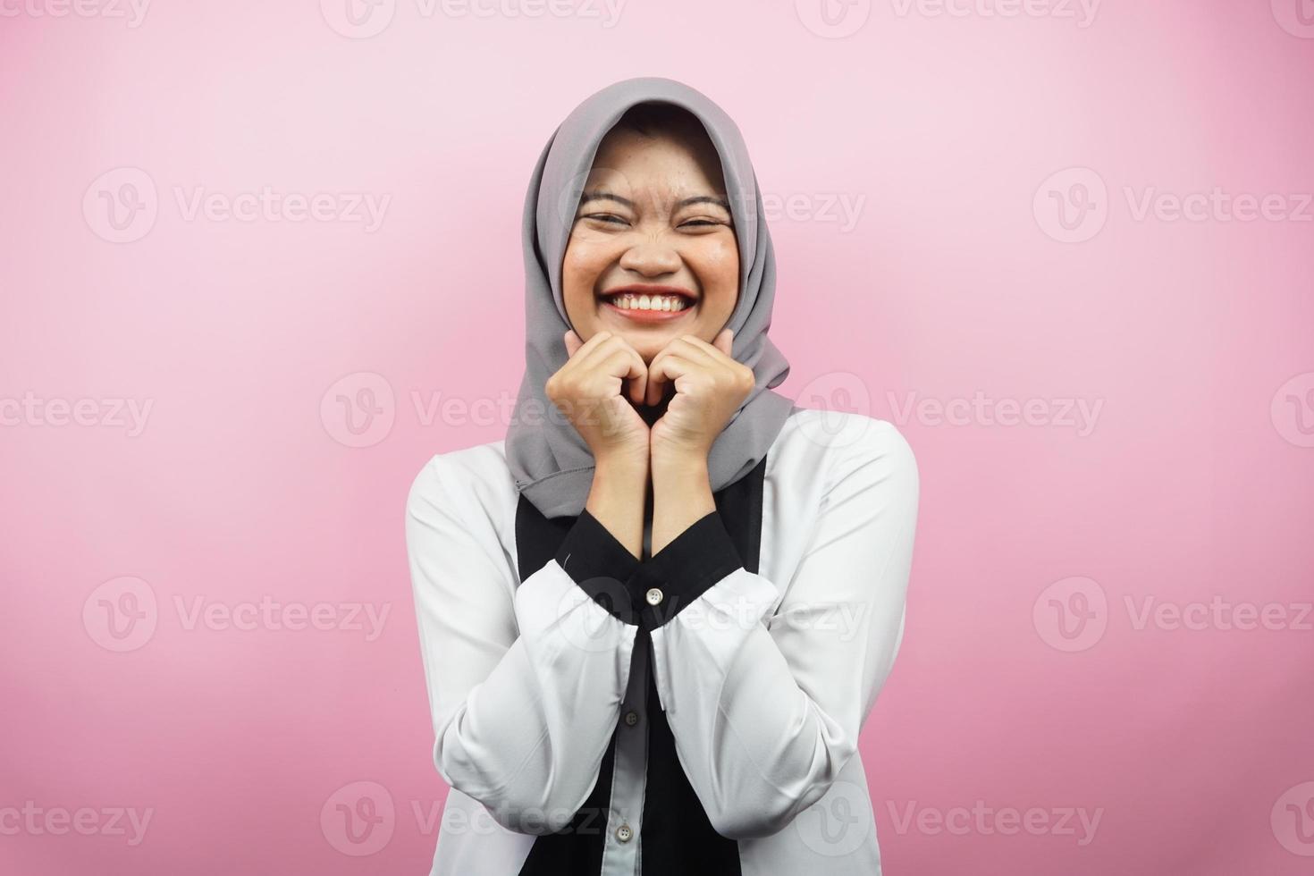 Hermosa joven musulmana asiática sonriendo feliz, linda, sintiéndose cómoda, sintiéndose cuidada, sintiéndose bien, con las manos sosteniendo la barbilla aislada sobre fondo rosa foto