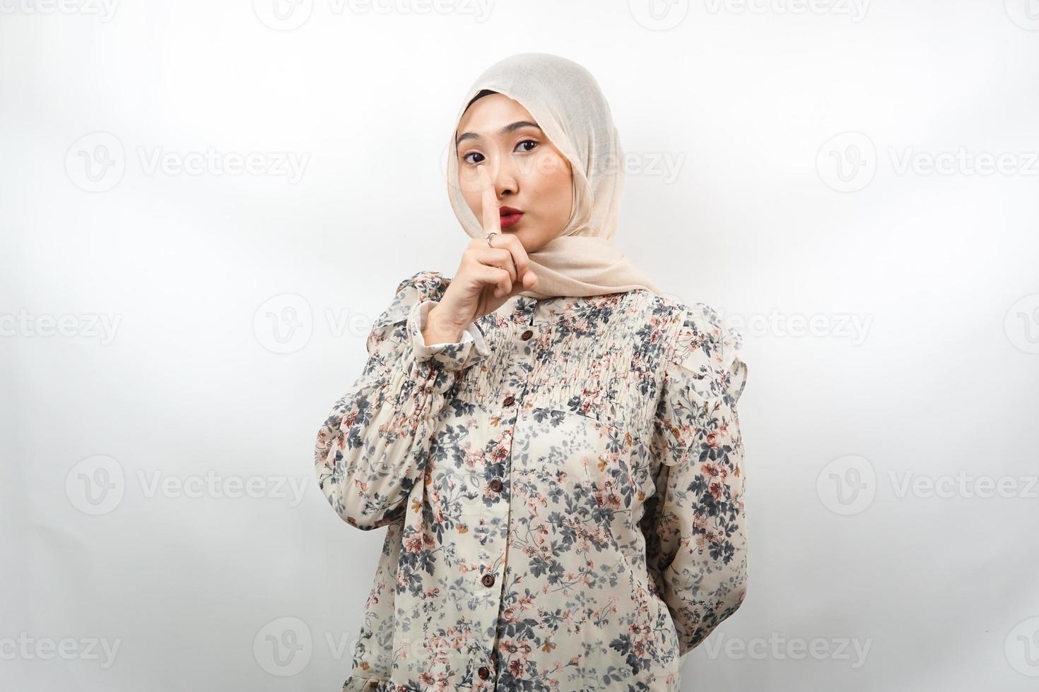 Beautiful asian young muslim woman with finger on mouth, telling to be quiet, don't make noise, lower your voice, don't talk, isolated on white background photo