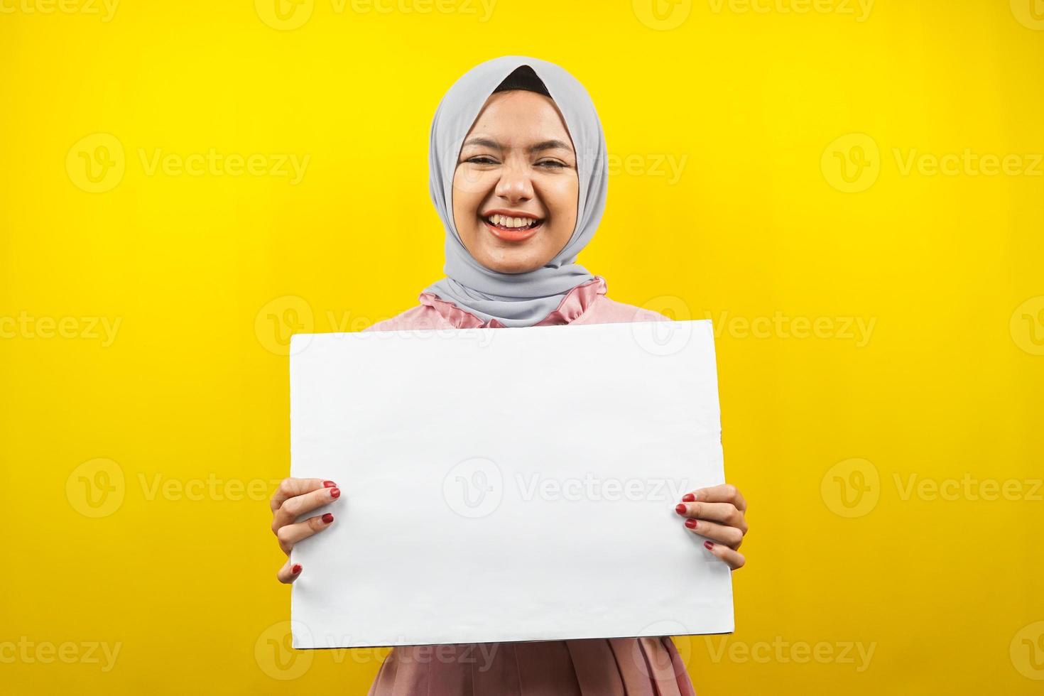 Bastante joven mujer musulmana alegre sosteniendo pancarta vacía en blanco, cartel, tablero blanco, tablero de letrero en blanco, tablero de anuncio blanco, presentando algo en el espacio de la copia, promoción foto