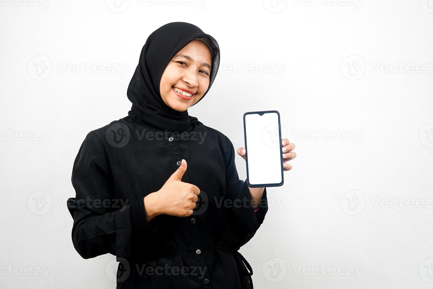 Hermosa joven musulmana asiática con las manos sosteniendo el teléfono inteligente, promoviendo la aplicación, sonriendo con confianza y entusiasmo, mano de signo ok, buen trabajo, éxito, aislado sobre fondo blanco. foto