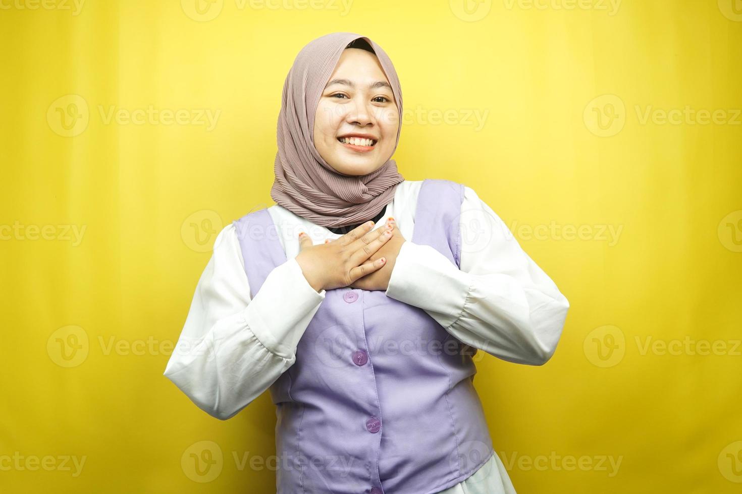 Hermosa joven mujer musulmana asiática sonriendo sorprendida y alegre, con las manos sosteniendo el pecho, emocionada, sin esperar, mirando a la cámara aislada sobre fondo amarillo foto