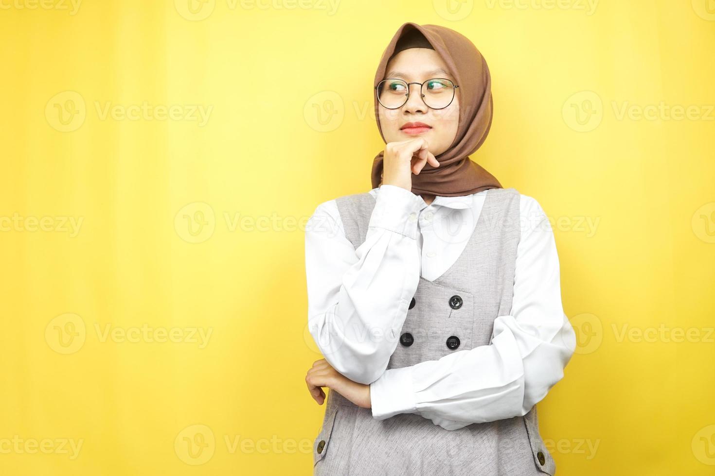 Beautiful asian young muslim woman thinking, there is a problem, feeling strange, something is wrong, looking for a solution, isolated on yellow background photo