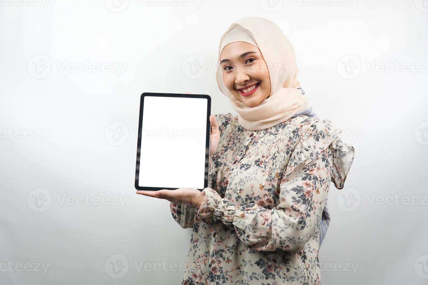 Hermosa joven musulmana asiática sonriendo, emocionada y alegre sosteniendo la tableta con pantalla blanca o en blanco, promocionando la aplicación, promocionando el producto, presentando algo, aislado sobre fondo blanco. foto