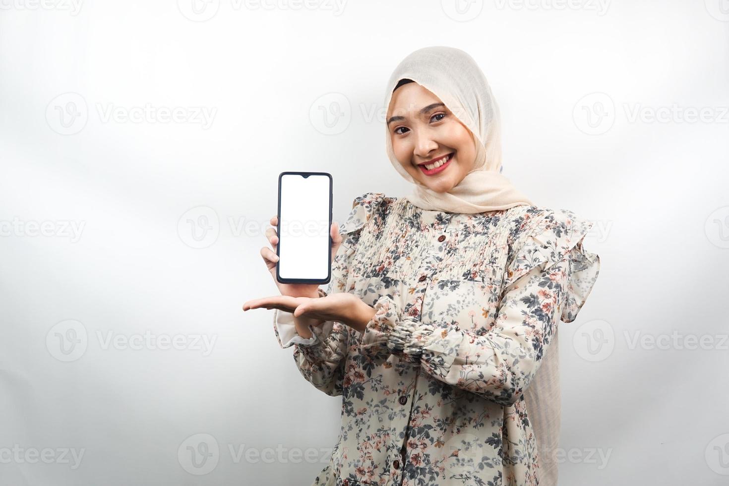 Beautiful young asian muslim woman smiling confidently and excitedly with hands holding smartphone, promoting app, promoting something, isolated on white background, advertising concept photo