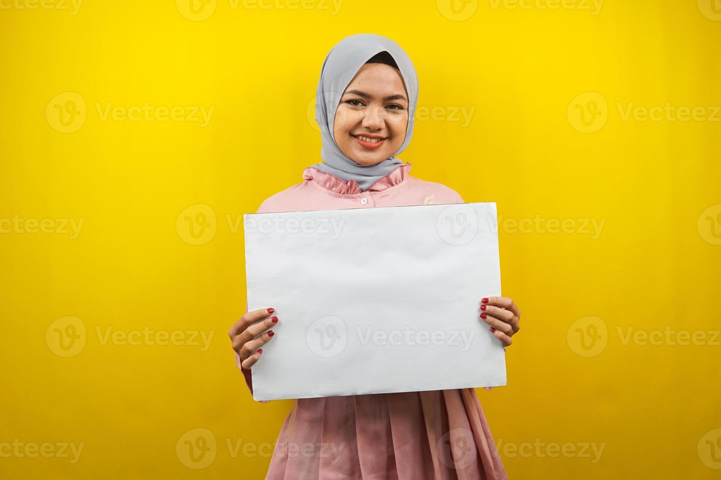 Bastante joven mujer musulmana alegre sosteniendo pancarta vacía en blanco, cartel, tablero blanco, tablero de letrero en blanco, tablero de anuncio blanco, presentando algo en el espacio de la copia, promoción foto