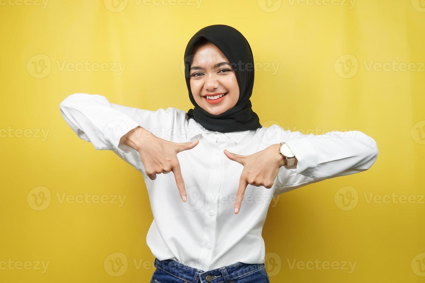 Hermosa joven musulmana asiática con las manos apuntando hacia abajo, las manos hacen clic en el enlace de abajo, las manos presentando algo, aislado sobre fondo amarillo foto