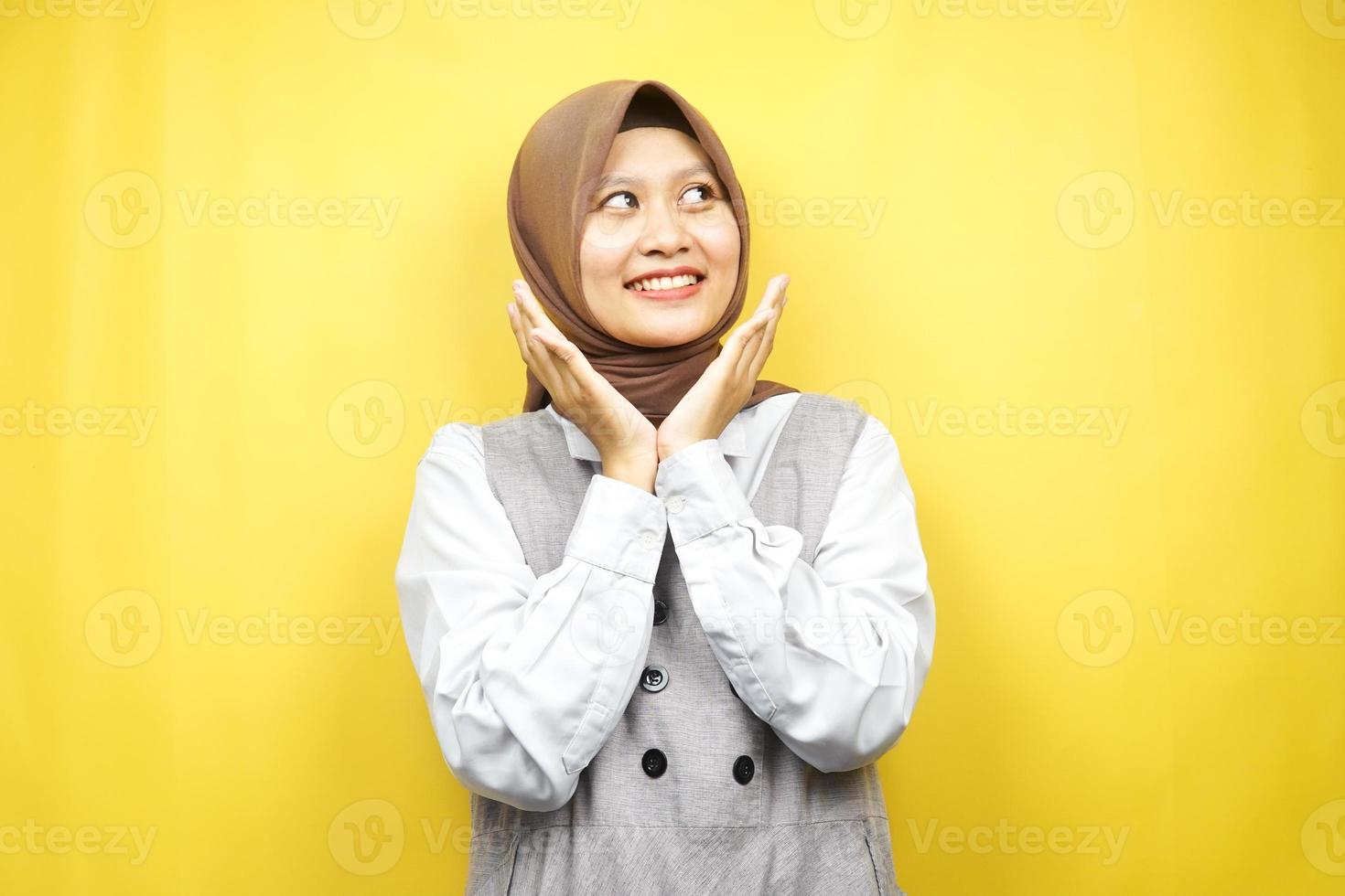 Beautiful young asian muslim woman smiling confident, enthusiastic and cheerful with hands V sign on chin isolated on yellow background photo