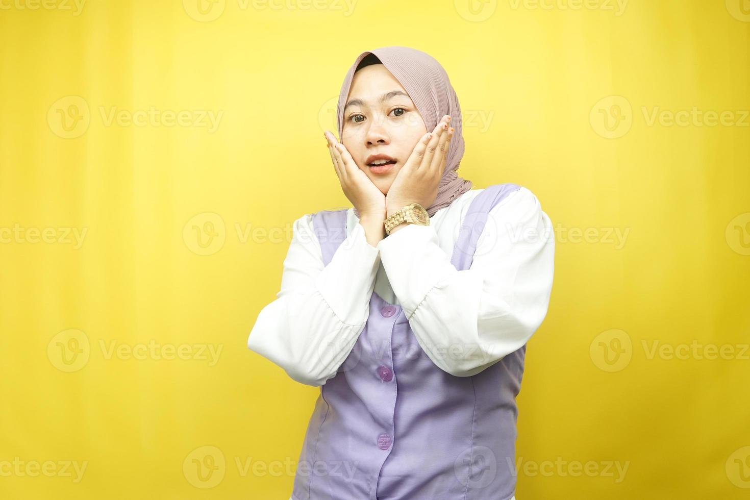 Hermosa joven mujer musulmana asiática conmocionada, sorprendida, expresión guau, con la mano que sostiene la mejilla frente a la cámara aislada sobre fondo amarillo foto