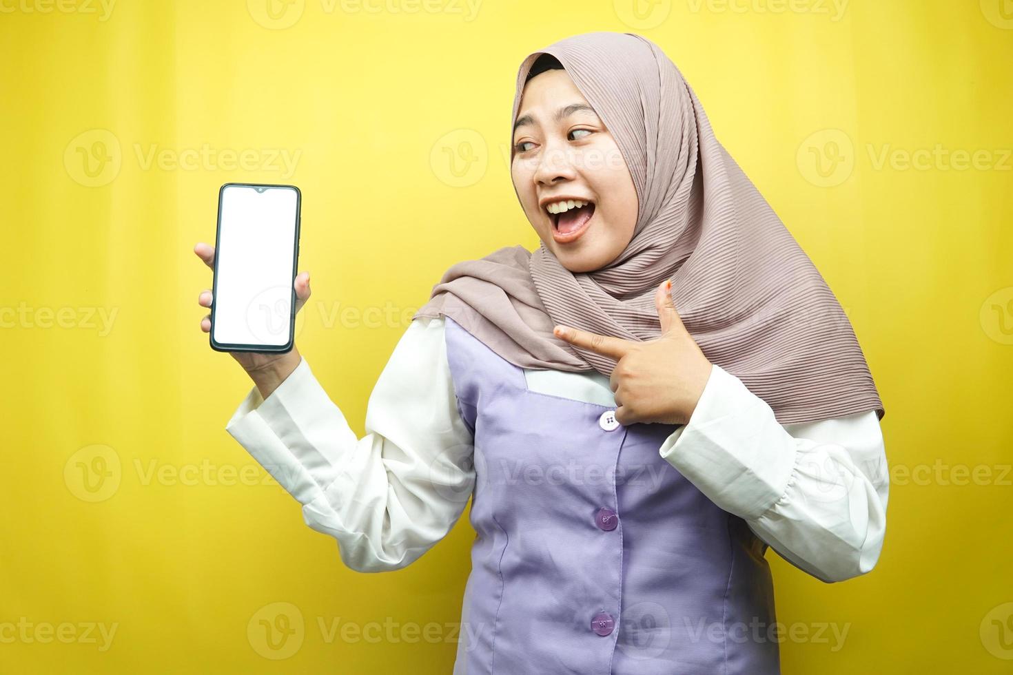 Hermosa joven mujer musulmana asiática conmocionada, sorprendida, expresión guau, mano sosteniendo un teléfono inteligente con pantalla blanca o en blanco, promocionando la aplicación, promocionando el producto, presentando algo, aislado foto