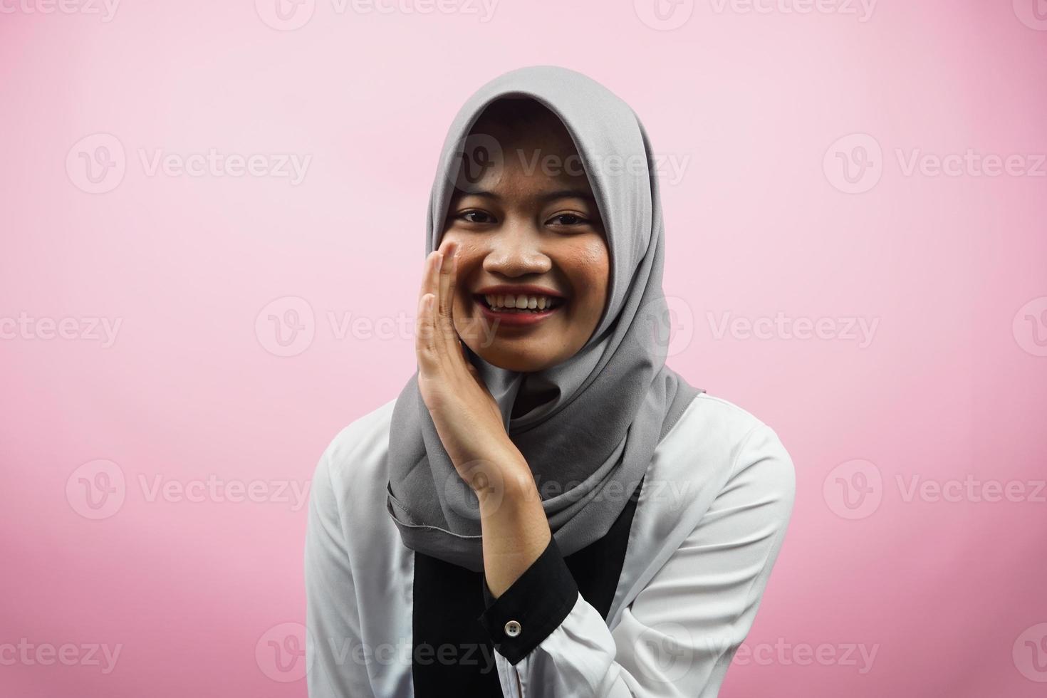 Beautiful young asian muslim woman smiling confidently and excitedly close to camera, whispering, telling secrets, speaking quietly, silent, isolated on pink background photo