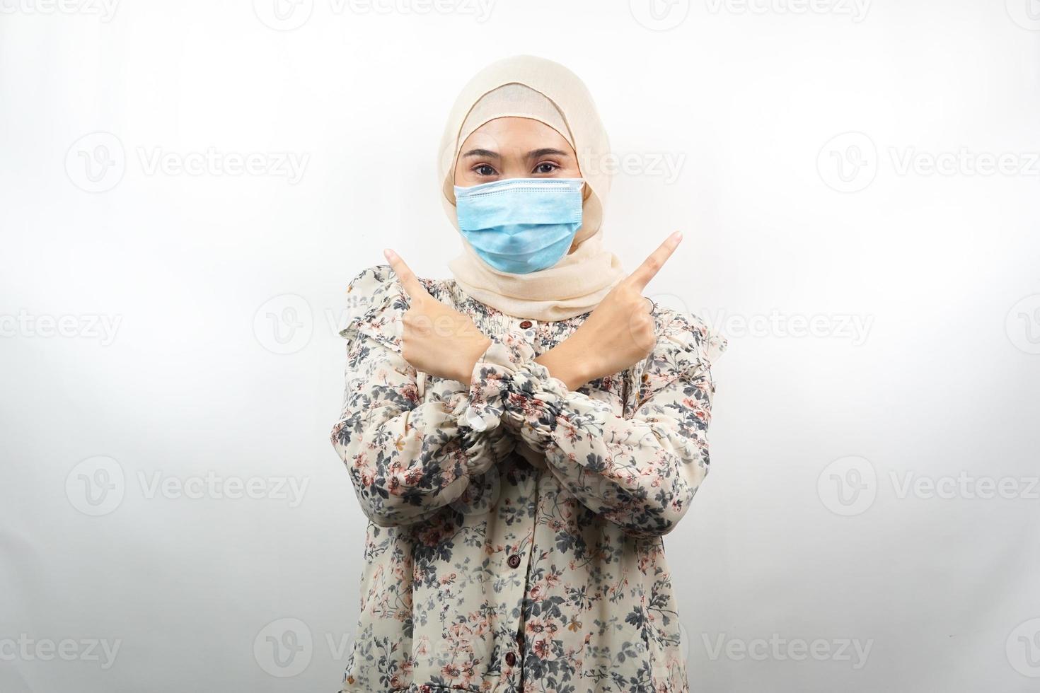 Mujer musulmana con máscara médica, mano apuntando al espacio vacío, mano apuntando hacia arriba presentando algo, aislado sobre fondo blanco. foto