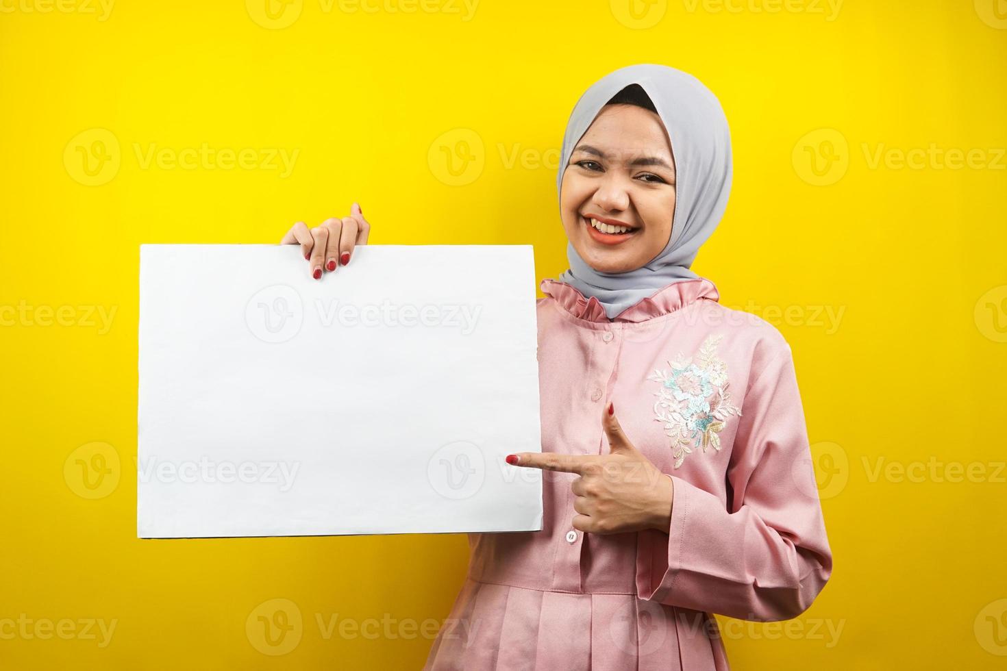 Bastante joven mujer musulmana alegre sosteniendo pancarta vacía en blanco, cartel, tablero blanco, tablero de letrero en blanco, tablero de anuncio blanco, presentando algo en el espacio de la copia, promoción foto