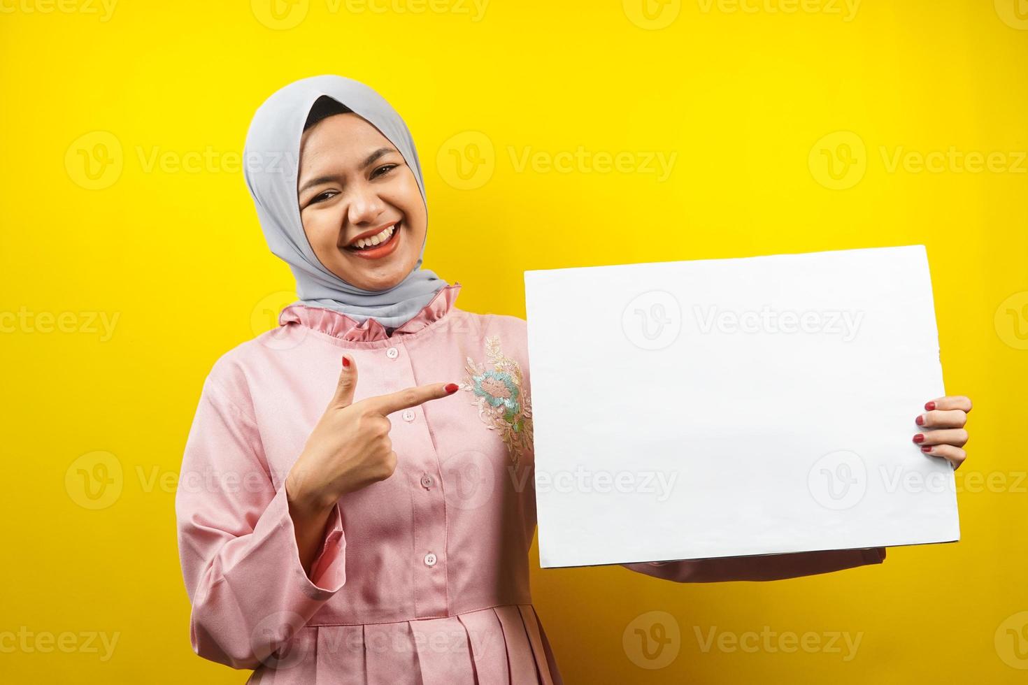 Bastante joven mujer musulmana alegre sosteniendo pancarta vacía en blanco, cartel, tablero blanco, tablero de letrero en blanco, tablero de anuncio blanco, presentando algo en el espacio de la copia, promoción foto