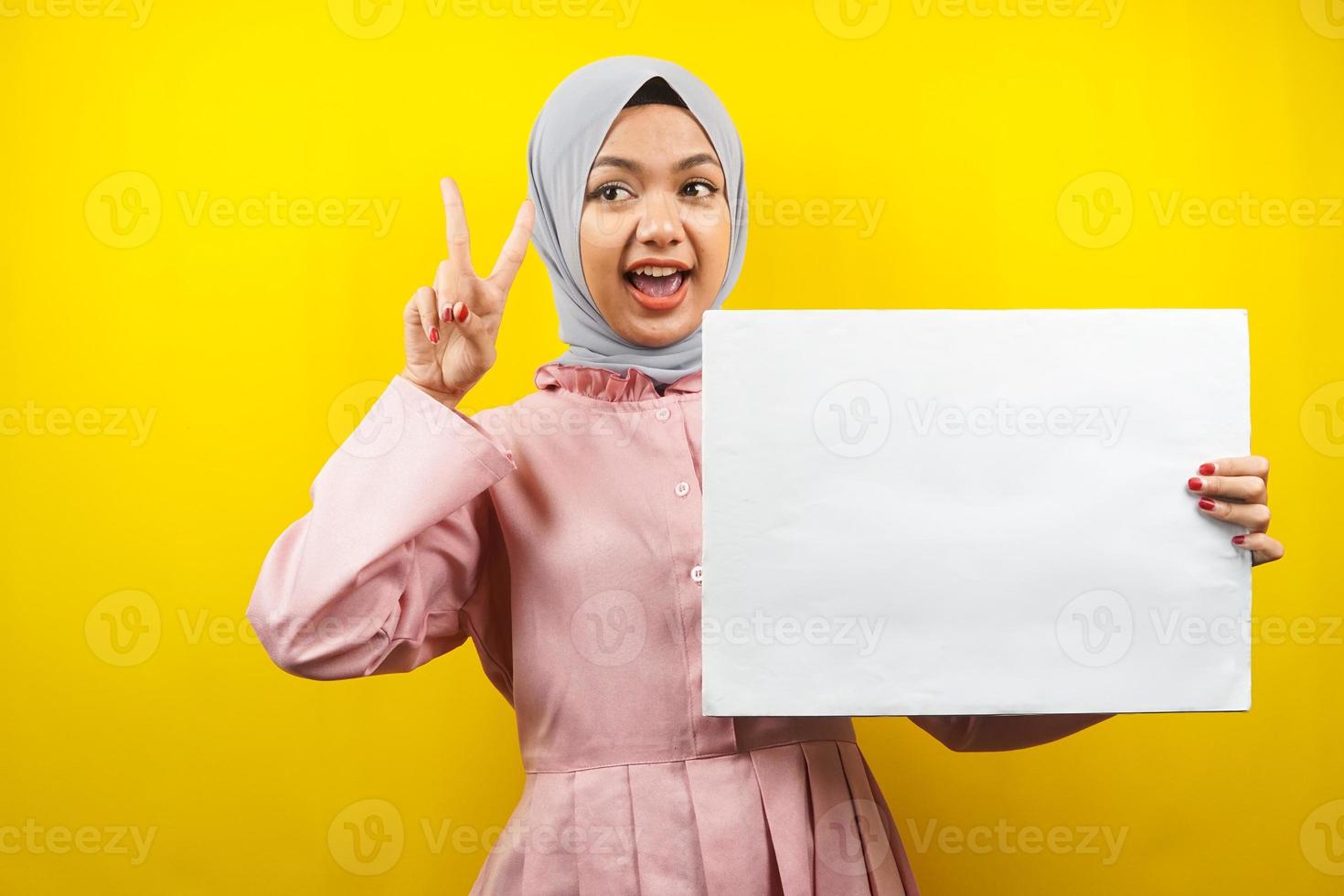 Bastante joven mujer musulmana alegre sosteniendo pancarta vacía en blanco, cartel, tablero blanco, tablero de letrero en blanco, tablero de anuncio blanco, presentando algo en el espacio de la copia, promoción foto