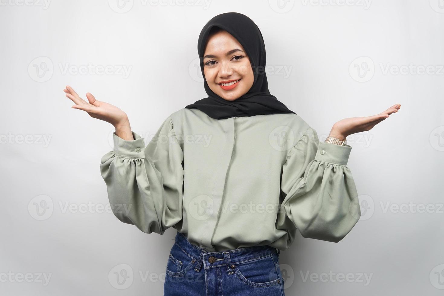 Hermosa joven musulmana asiática confiada y sonriente, con los brazos abiertos, presentando algo, presentando producto, aislado sobre fondo gris foto