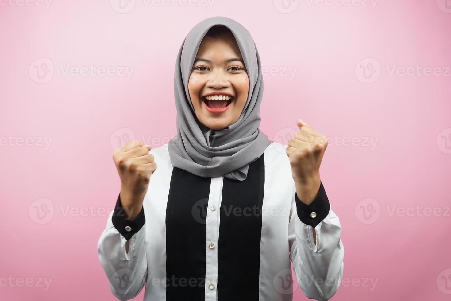 Beautiful young asian muslim woman smiling confident, enthusiastic and cheerful with  hands clenched, sign of success, punching, fighting, not afraid, isolated on pink background photo