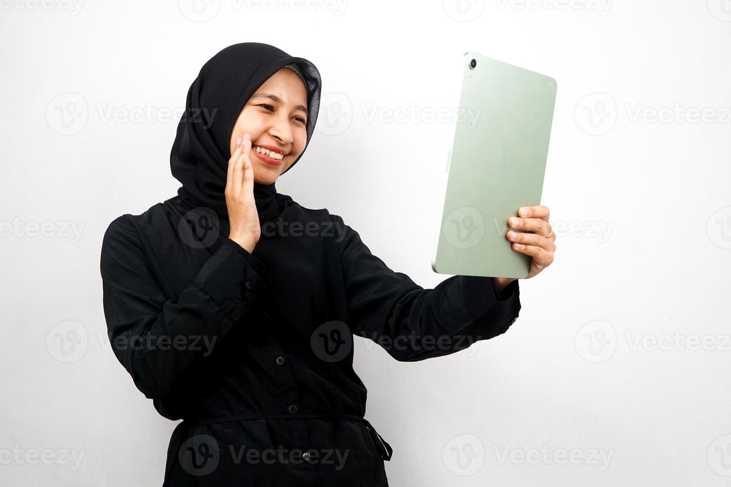 Beautiful young asian muslim woman smiling, excited and cheerful holding tablet, isolated on white background photo