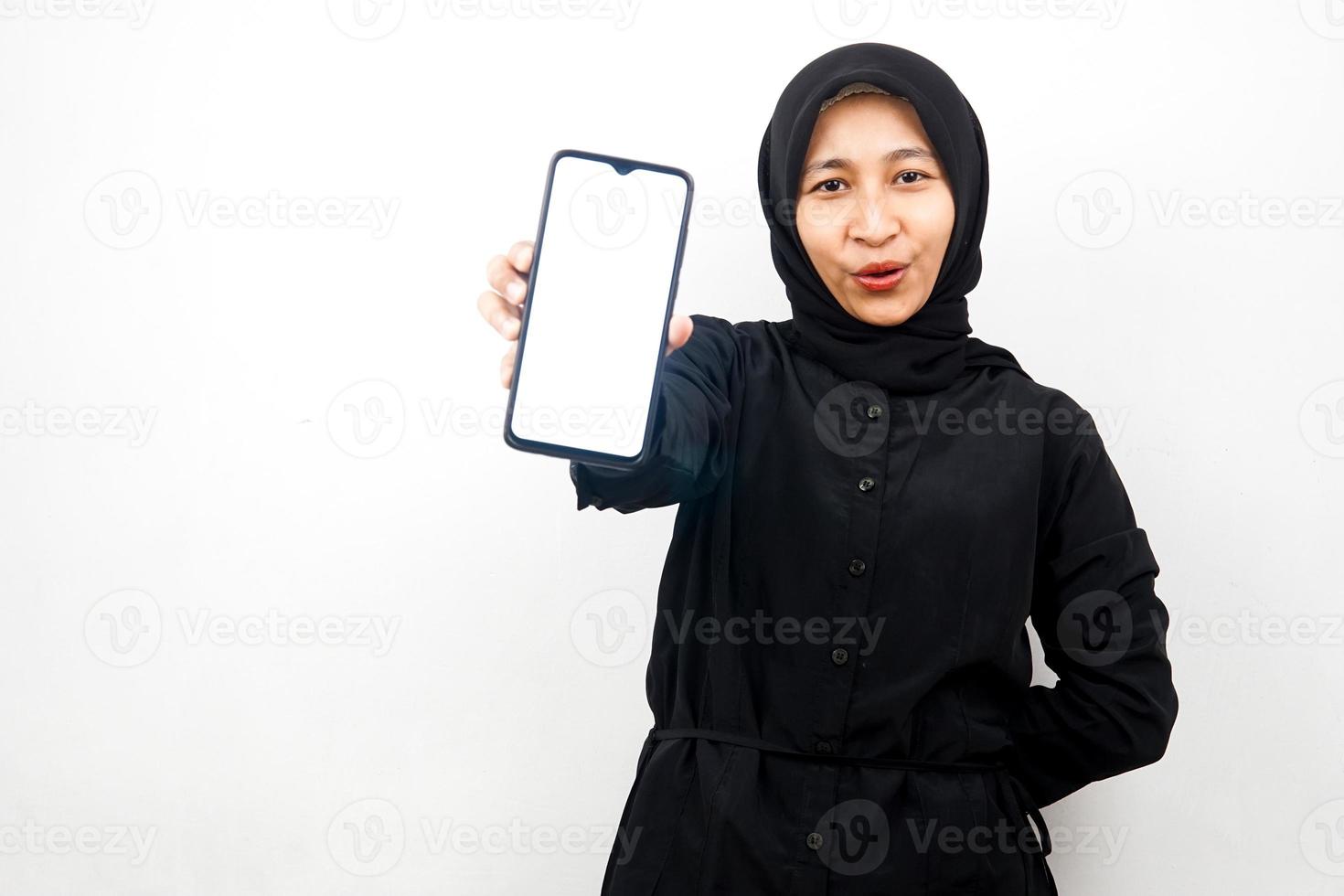 Hermosa joven mujer musulmana asiática conmocionada, sorprendida, expresión guau, mano sosteniendo un teléfono inteligente con pantalla blanca o en blanco, promocionando la aplicación, promocionando el producto, presentando algo, aislado foto