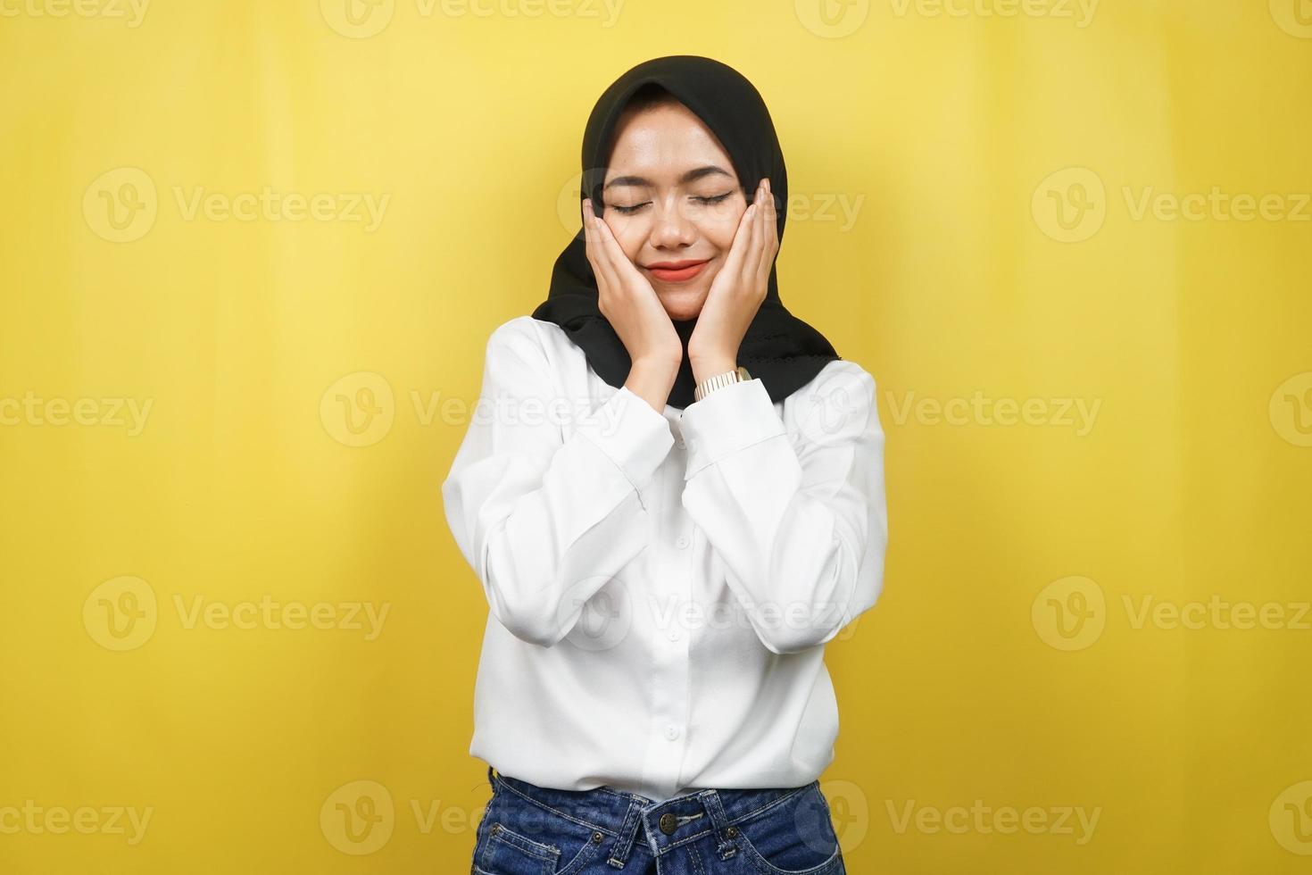 Beautiful young asian muslim woman smiling happy, cute, feeling comfortable, feeling cared for, feeling good, with  hands holding cheeks isolated on yellow background photo