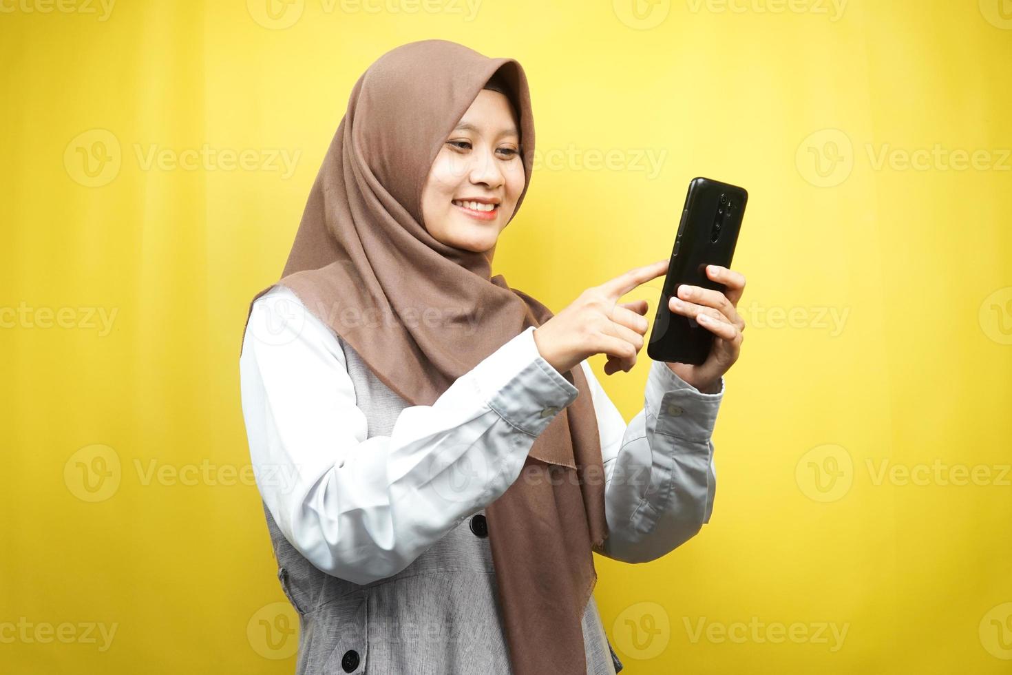 Hermosa joven mujer musulmana asiática sonriendo con confianza sosteniendo smartphone aislado sobre fondo amarillo, concepto de publicidad foto