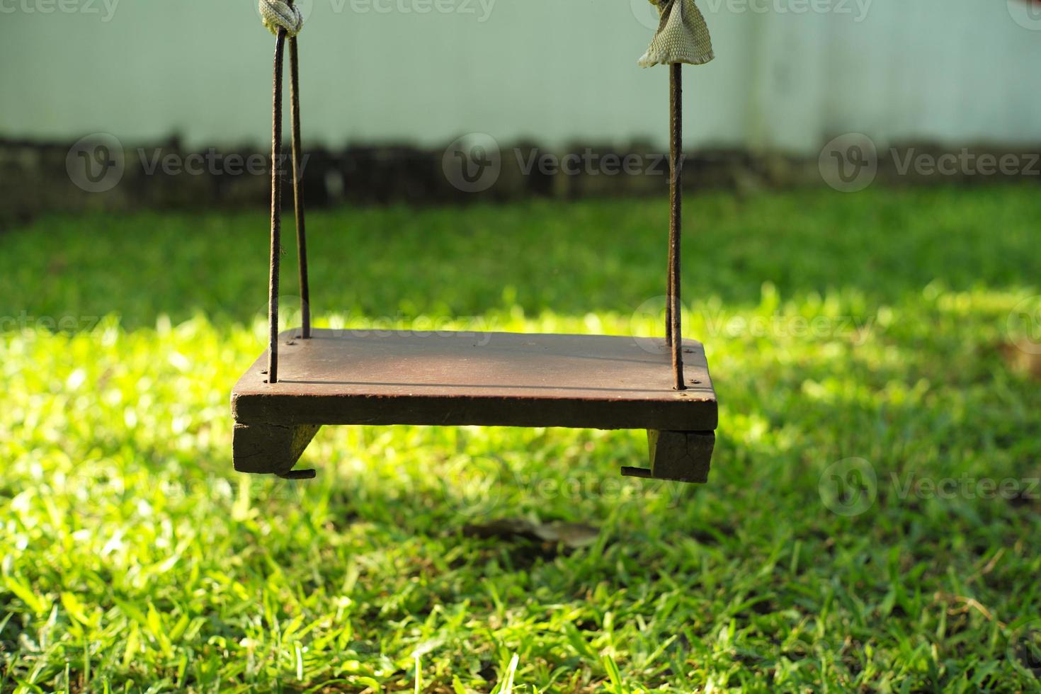 Closeup old wooden swing hanging from the tree in the backyard garden photo