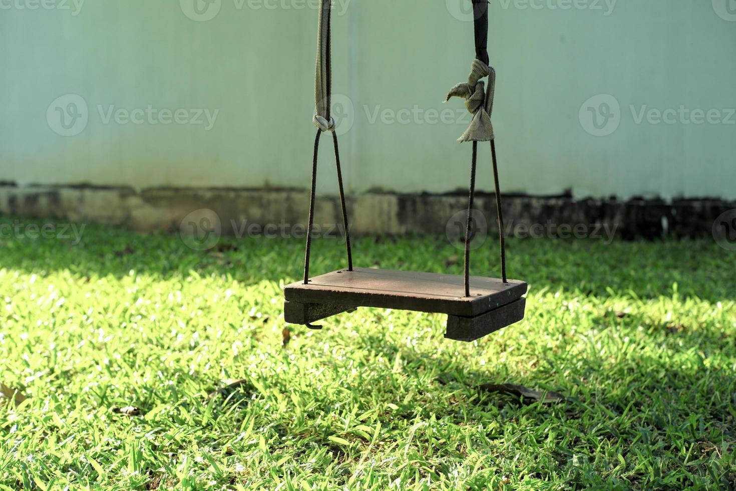 Closeup old wooden swing hanging from the tree in the backyard garden photo