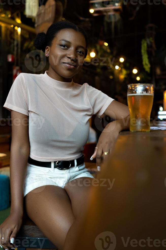 Joven mujer negra con peinado afro mirando a la cámara sentado en un bar. foto