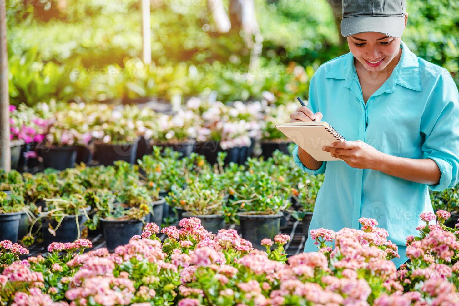 Happy young woman working in a greenhouse, writing notes and studying the growth of trees. photo