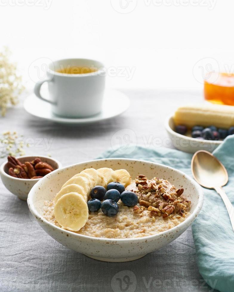 avena integral, tazón grande de avena con plátano, frutos del bosque, nueces para el desayuno. vista lateral, vertical foto