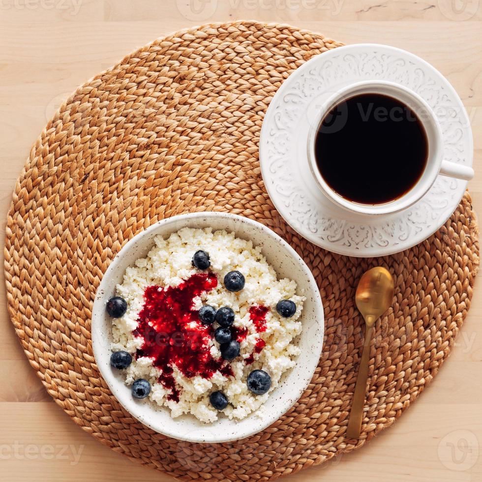 White bowl of homemade curd with jam, raspberries, blueberries and cup of coffee photo